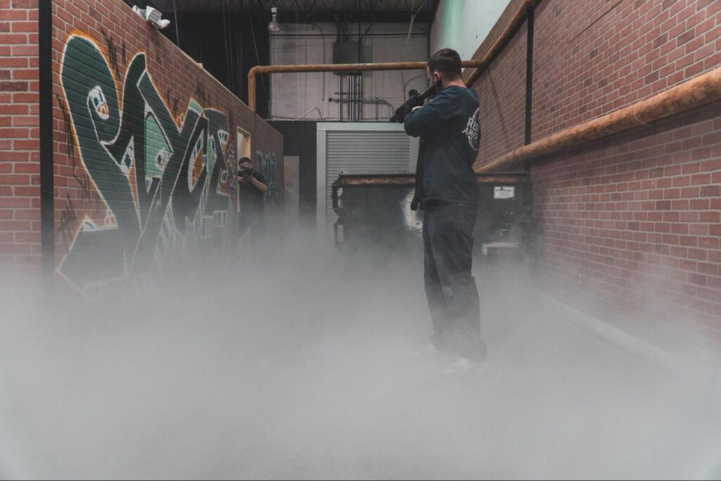 Two people stand in a corridor with brick walls and graffiti, facing each other through a haze of smoke—an edgy setting perfect for unique team building activities inside an industrial-style building.