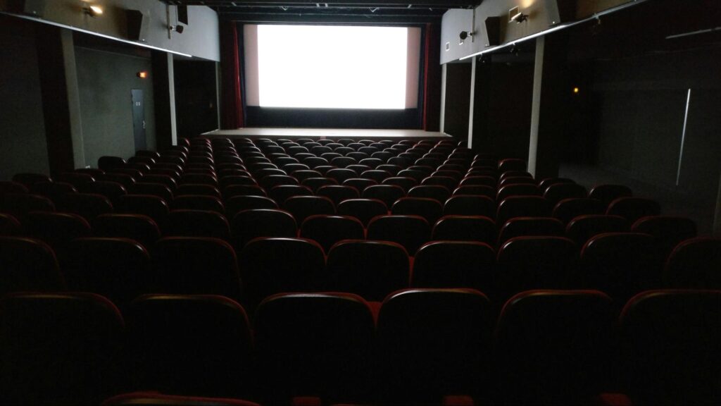 Popular movie theater with rows of seats facing a large, brightly lit screen at the front of the room, perfect for a summer day in New Jersey.