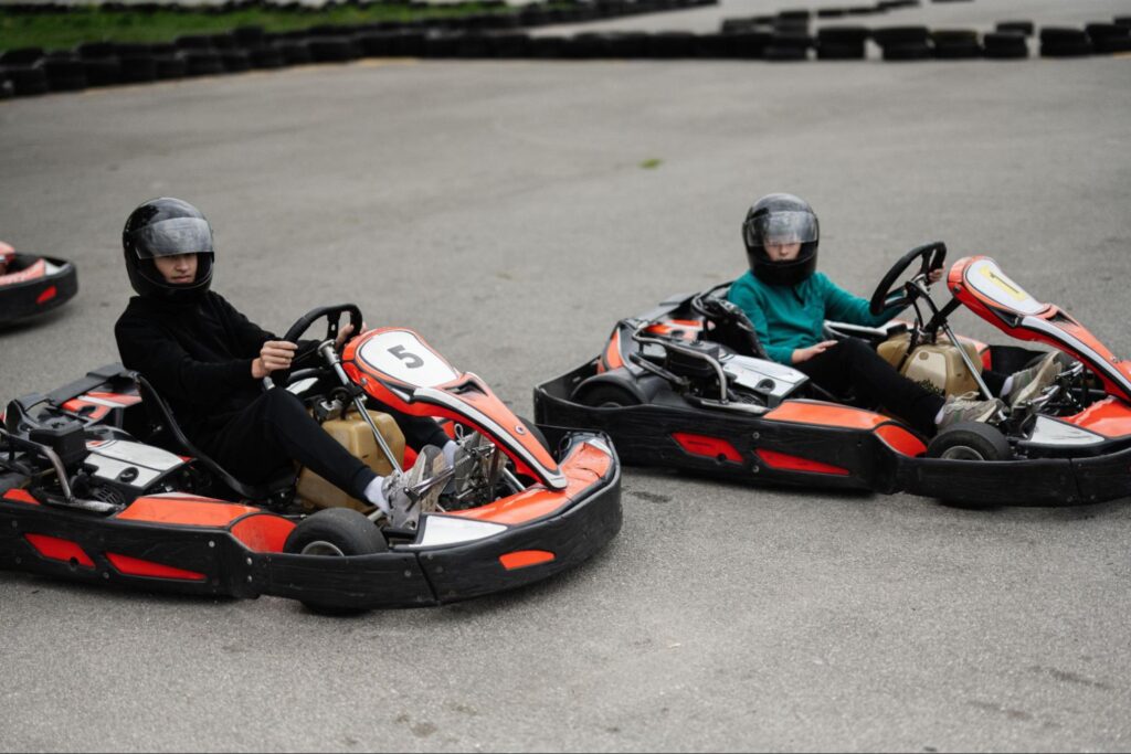 Two people in helmets and casual clothing sit in red and black go-karts on a paved track at Tac Ops NJ, preparing to race—perfect for those seeking unique corporate event ideas.