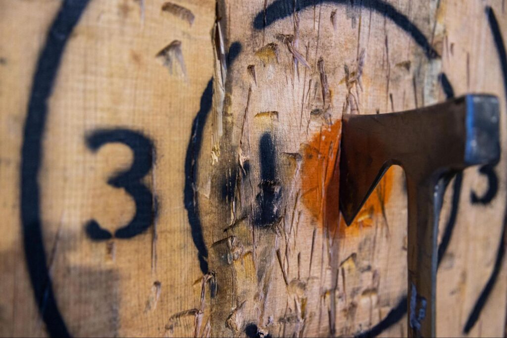 A hatchet is embedded in the center of a wooden target marked with black rings and the number 3, making it a thrilling option for Indoor Summer Activities in Fairfield NJ to beat the heat.