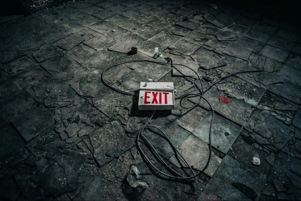 A fallen exit sign lies on a cracked, debris-strewn floor in New Jersey, with loose cables and broken tiles visible around it.