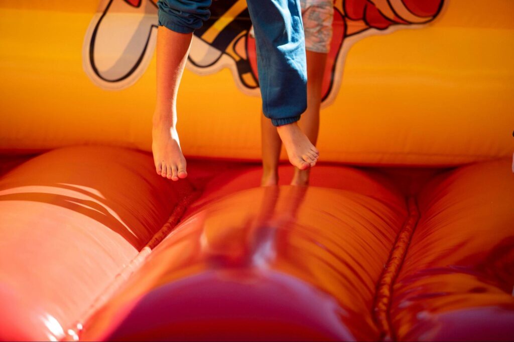 Two children are jumping barefoot on a red and orange inflatable bounce house, with only their lower legs and feet visible—a fun scene perfect for indoor birthday parties or anyone seeking birthday party ideas for kids in New Jersey.