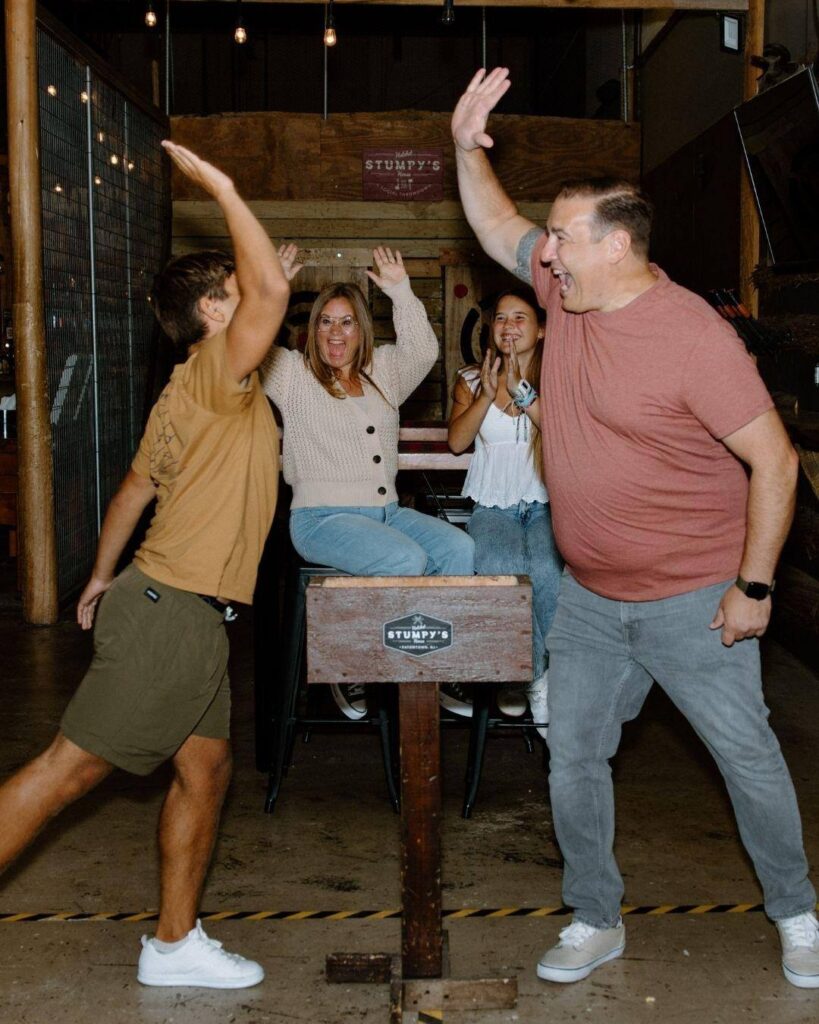 Two people high-five in front of a wooden table while two others sit behind them, smiling and clapping, capturing the spirit of indoor fun in a casual setting—perfect for birthday party ideas.