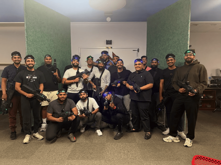 A group of people pose indoors holding laser tag guns and wearing headbands, standing in front of green partitions and office furniture—perfect for a fun Halloween date night or creative Halloween ideas in New Jersey.