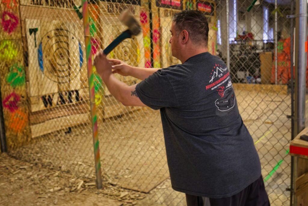 A man wearing a dark T-shirt is throwing an axe toward a wooden target inside an indoor axe-throwing facility, one of New Jersey's top fun date ideas.