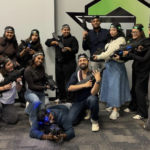 A group of people pose indoors wearing headbands and holding laser tag guns, with one person lying on the floor in front—an energetic scene that's perfect for those seeking fun corporate event ideas in New Jersey.
