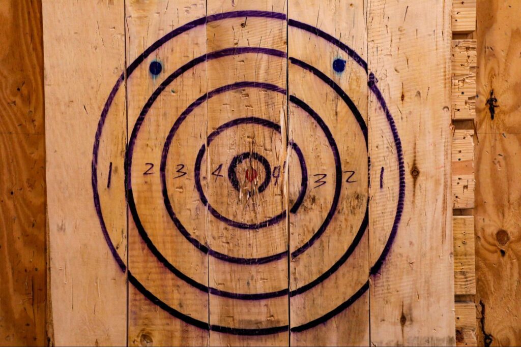 Wooden target board with concentric black circles, numbers 1 to 4, and two small blue dots near the outer ring—perfect for axe or knife throwing at the best corporate events in New Jersey.