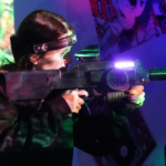 A person aims a laser tag gun while wearing a headband sensor in a room with colorful lights—perfect for group experience and tactical laser tag sessions, making it an exciting activity for summer camps.